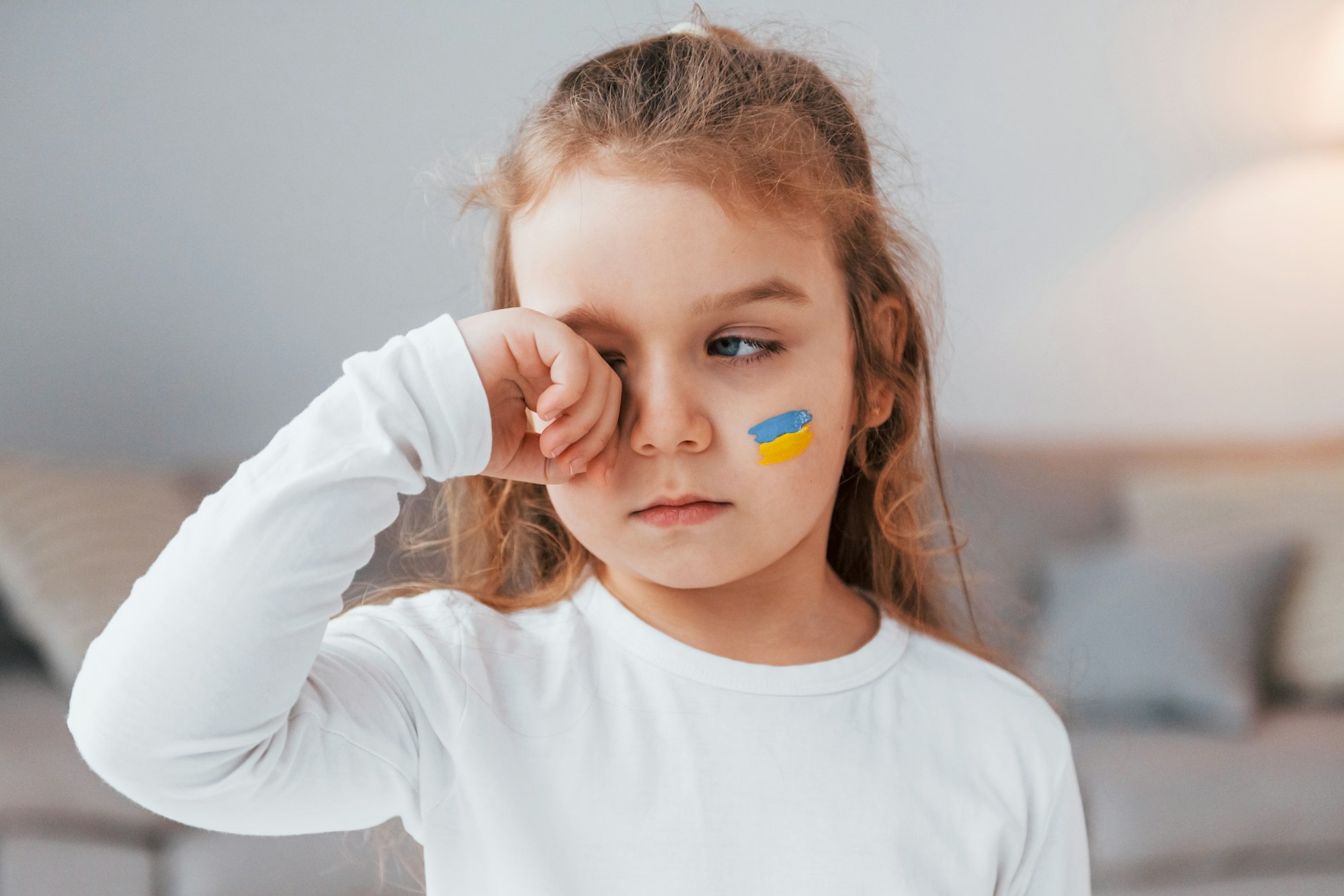 Innocent child is crying. Portrait of little girl with Ukrainian flag make up on the face